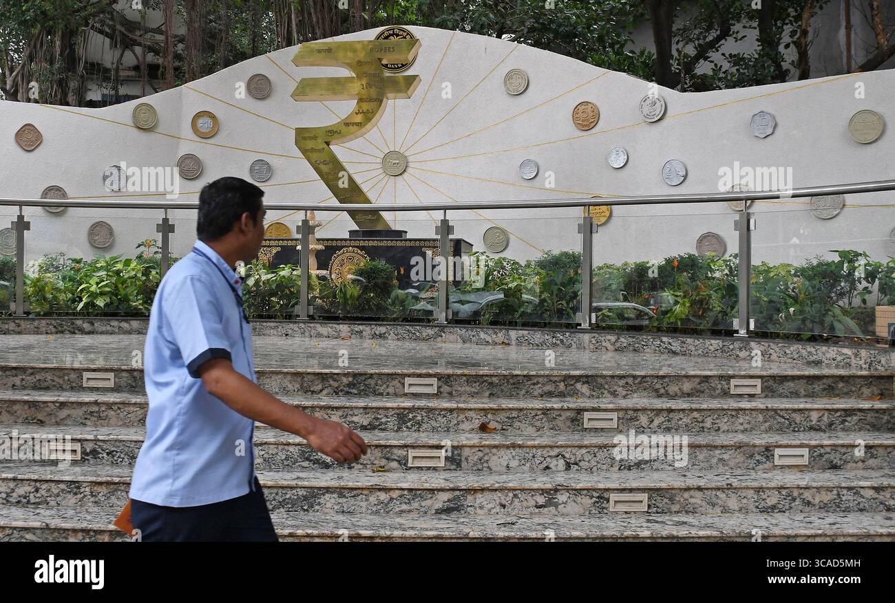 Un homme passe devant une installation de symboles de roupies devant le bâtiment de la Reserve Bank of India (RBI) à Mumbai. Le symbole de la roupie est la monnaie officielle de l'Inde utilisée dans toutes les transactions financières de biens et services à travers le pays. Banque D'Images