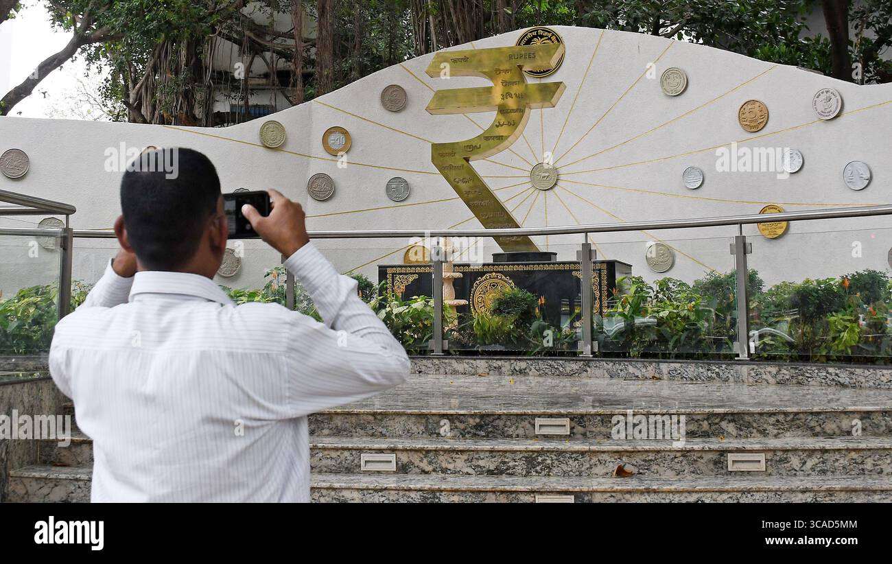 Un homme prend une photo de l'installation du symbole de la roupie avec son téléphone portable devant le bâtiment de la Reserve Bank of India (RBI) à Mumbai. Le symbole de la roupie est la monnaie officielle de l'Inde utilisée dans toutes les transactions financières de biens et services à travers le pays. Banque D'Images