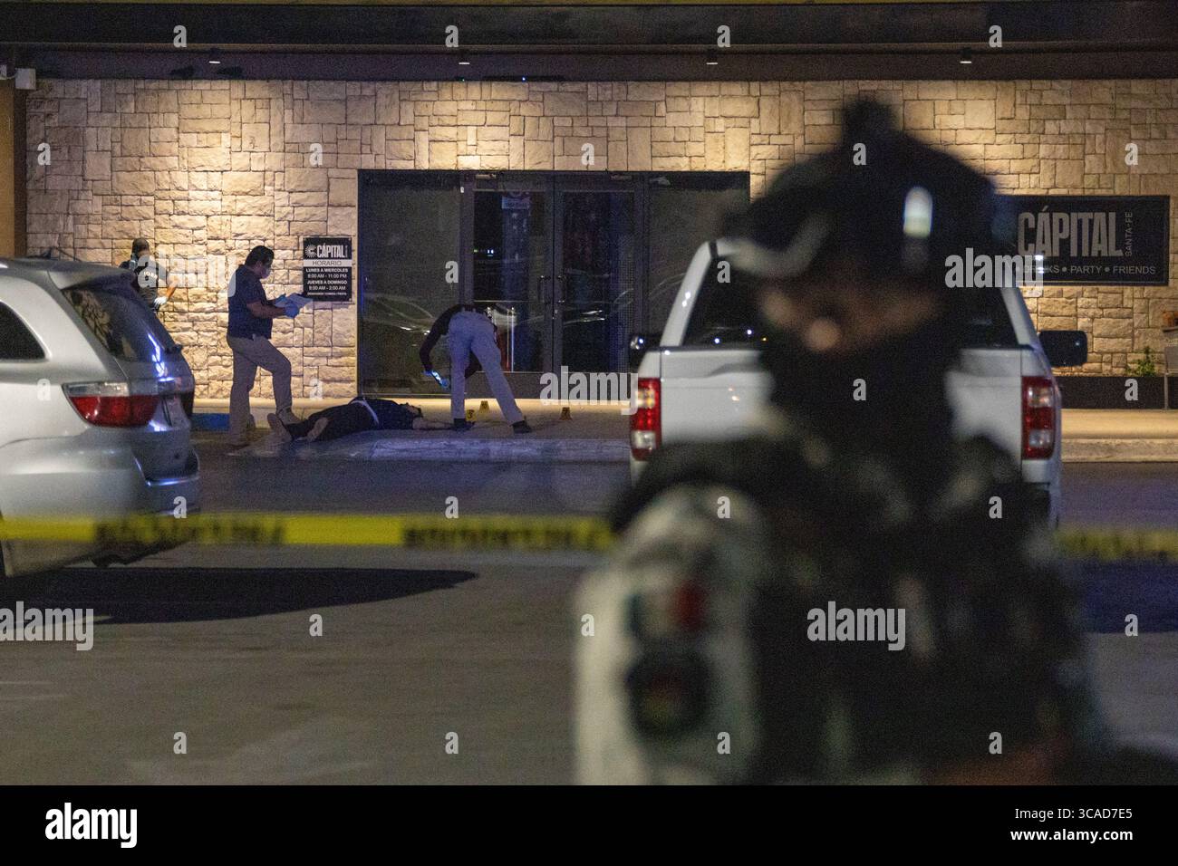 Police et civils sur une scène de crime à Ciudad Juarez, marquée par une bande jaune sous le ciel nocturne sombre. Banque D'Images