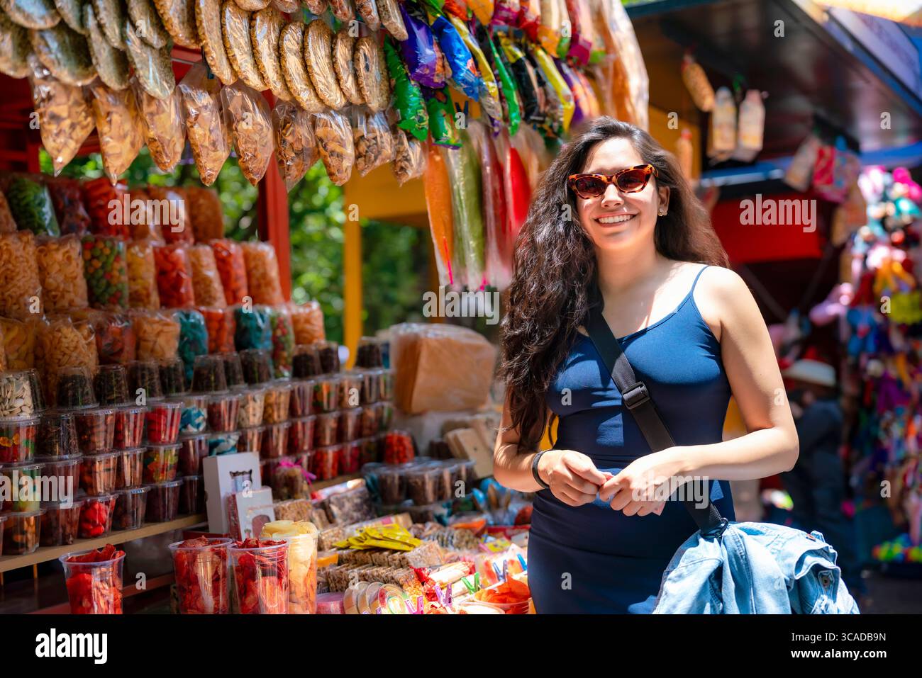 Une jeune femme latina souriante visite un étal coloré de nourriture de rue mexicaine plein de collations, de bonbons, de beignets croustillants et de friandises traditionnelles à Chapultepec, me Banque D'Images