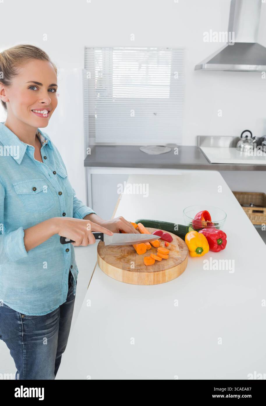 Femme tranchant des carottes sur une planche à découper au comptoir de la cuisine avec des poivrons, courgettes, espace de copie Banque D'Images