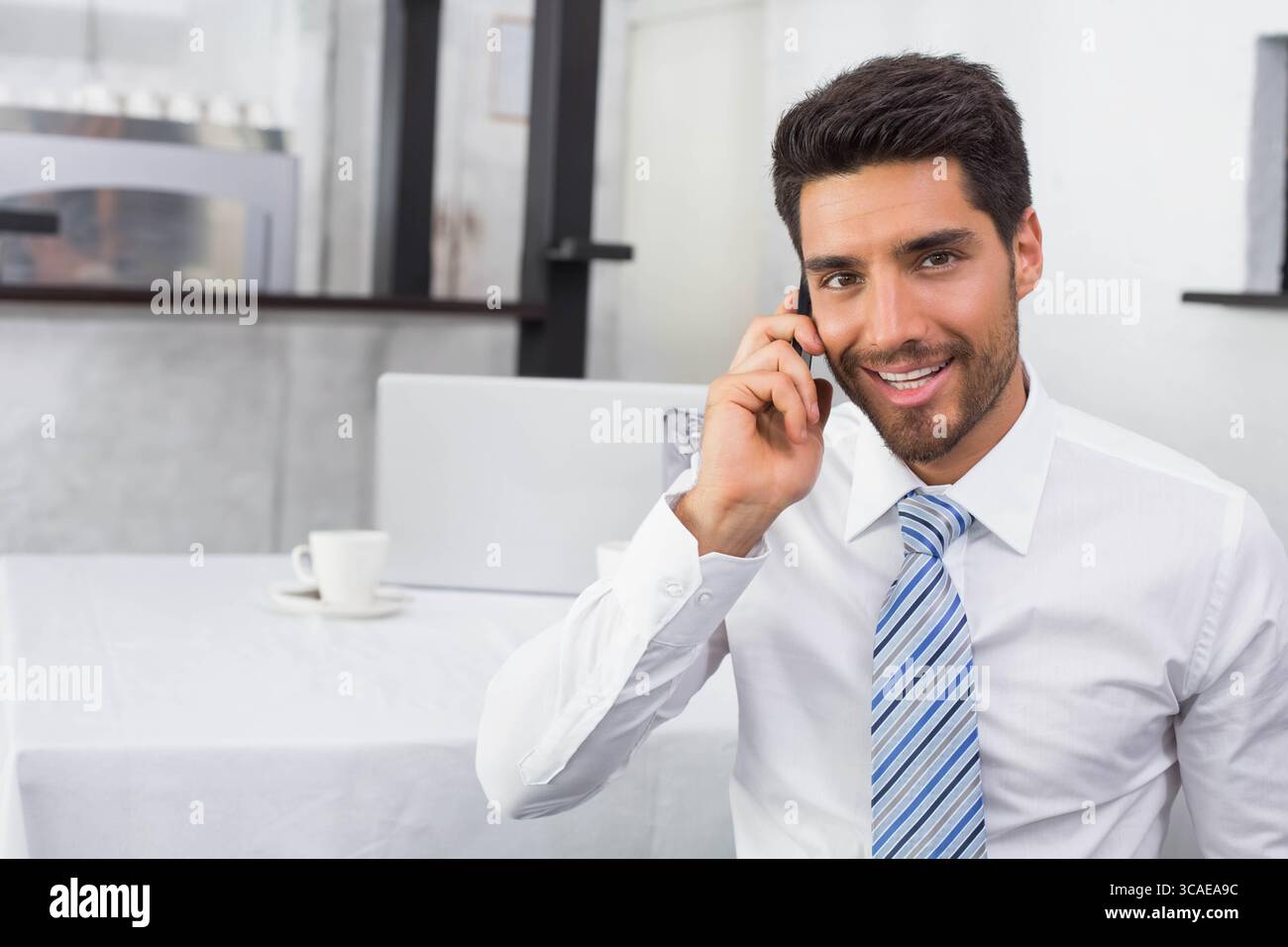 Homme d'affaires assis au café parlant sur smartphone avec ordinateur portable, tasse à café, espace de copie Banque D'Images
