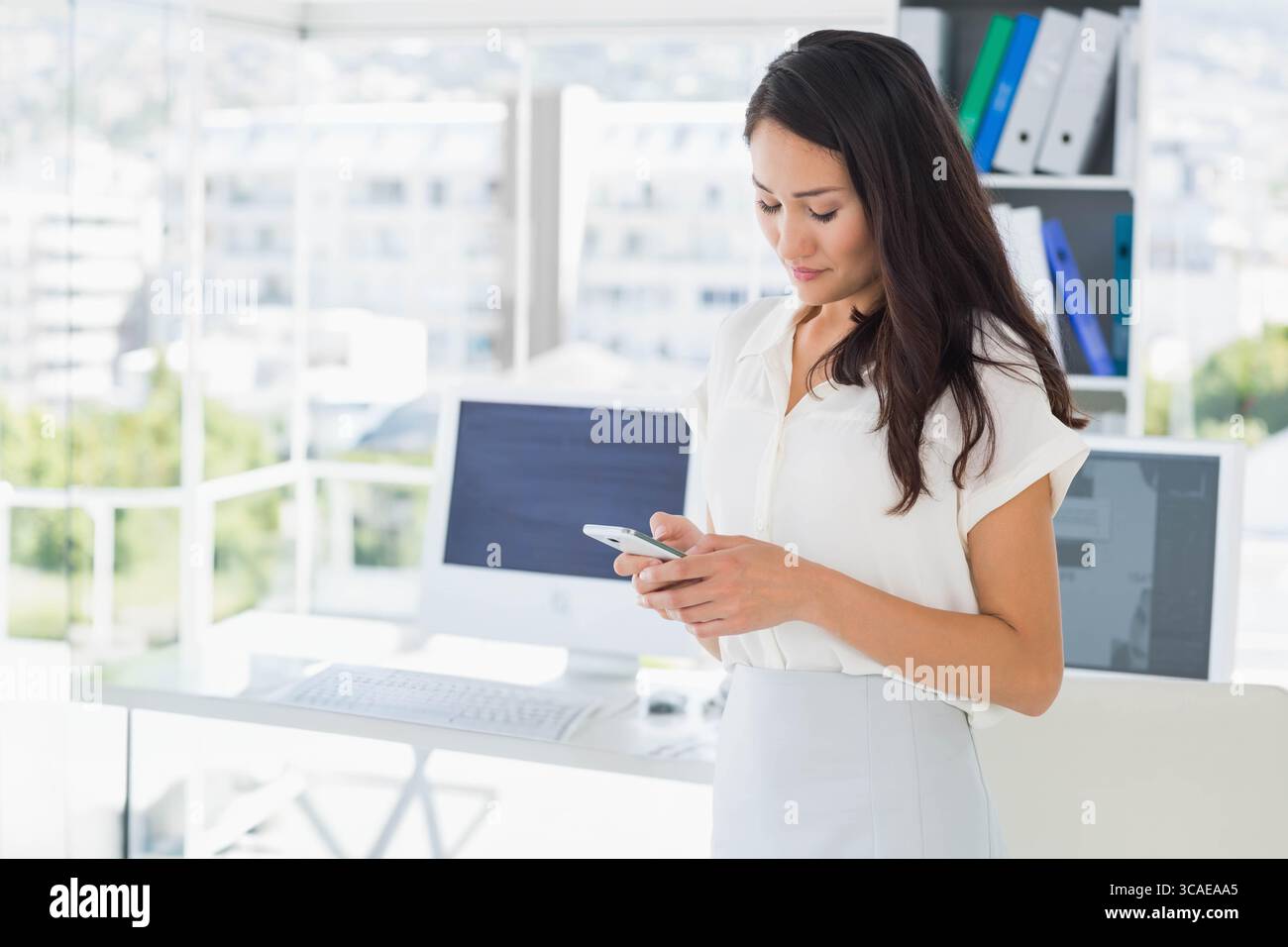 Femme asiatique vérifiant smartphone dans le bureau portant une tenue d'affaires près du bureau et du moniteur, espace de copie Banque D'Images