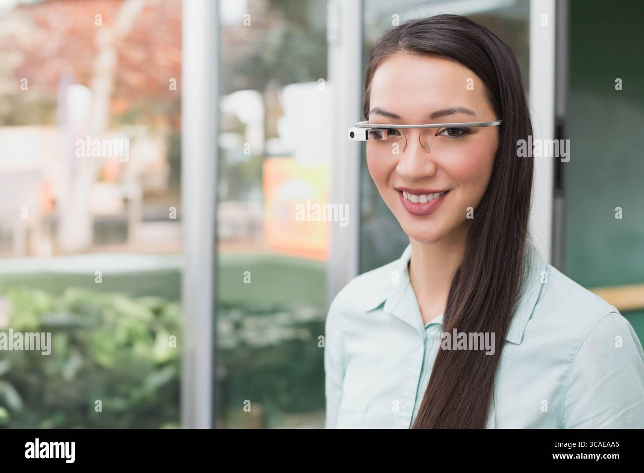 Femme asiatique debout à l'intérieur du hall de bureau moderne en utilisant des lunettes intelligentes près de grands panneaux de verre Banque D'Images