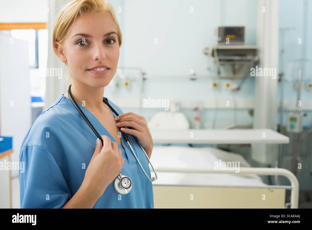 Infirmière debout à l'hôpital tenant le stéthoscope près du lit, moniteur et panneau de gaz, espace de copie Banque D'Images