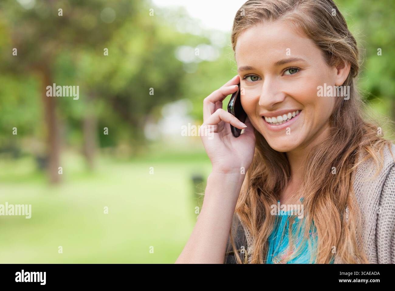 Femme parlant sur smartphone à l'oreille tout en se tenant dans le parc portant le dessus turquoise, espace de copie Banque D'Images