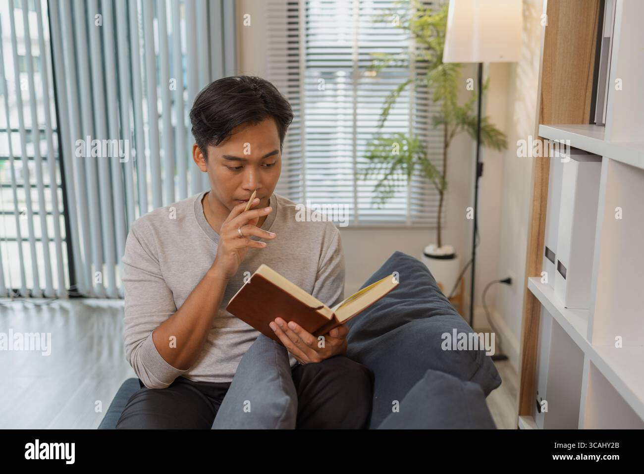 Un jeune homme se détache sur un canapé, lisant un livre avec une expression calme. Il aime le temps calme et la détente personnelle, trouver la paix et le confort whil Banque D'Images