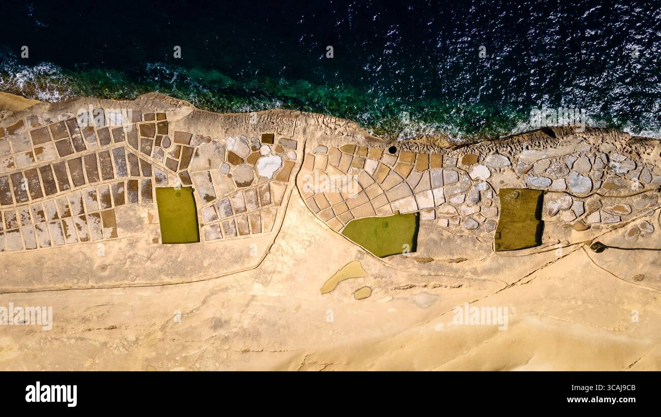 Vue aérienne de haut en bas des marais salants traditionnels sculptés dans la côte calcaire de Gozo, Malte, avec de l'eau méditerranéenne turquoise. Banque D'Images