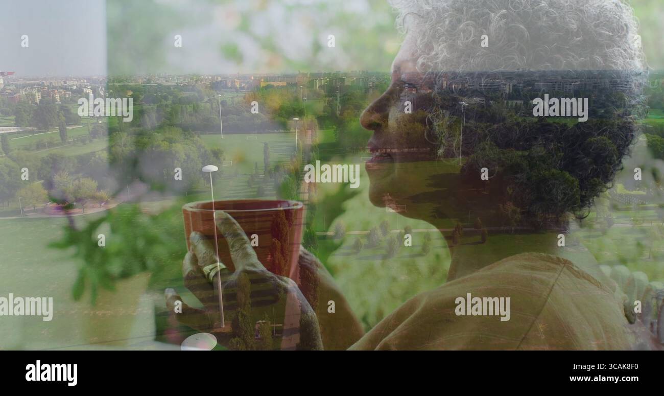 Tenant tasse en céramique rouge, femme senior regardant à travers la fenêtre du balcon à la maison, vue sur le parc, espace de copie Banque D'Images