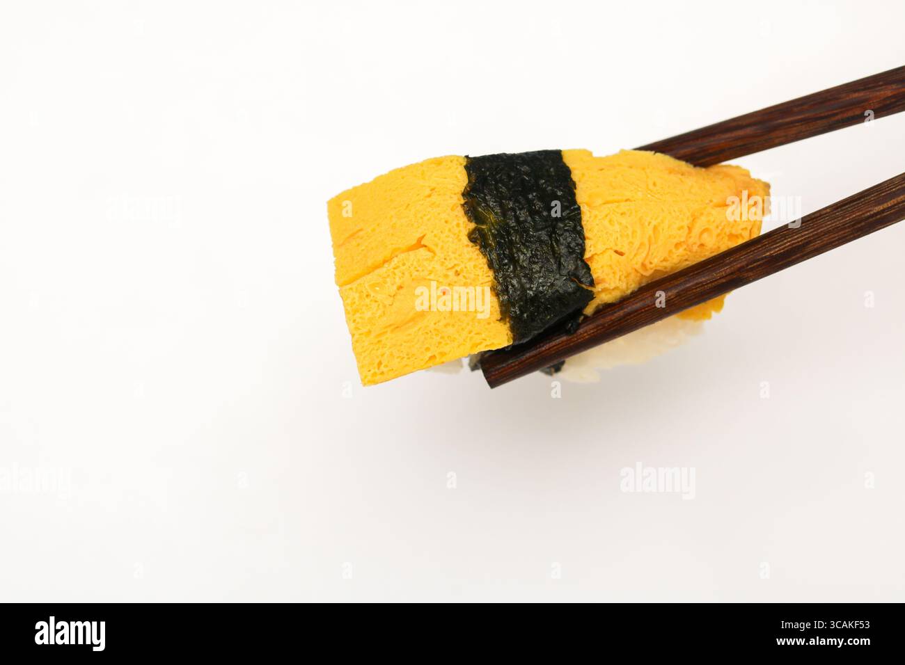 Un morceau de sushi Tamago Nigiri, représentant un œuf japonais sur un lit de riz et fixé avec une bande de nori, délicatement tenue par des baguettes Banque D'Images