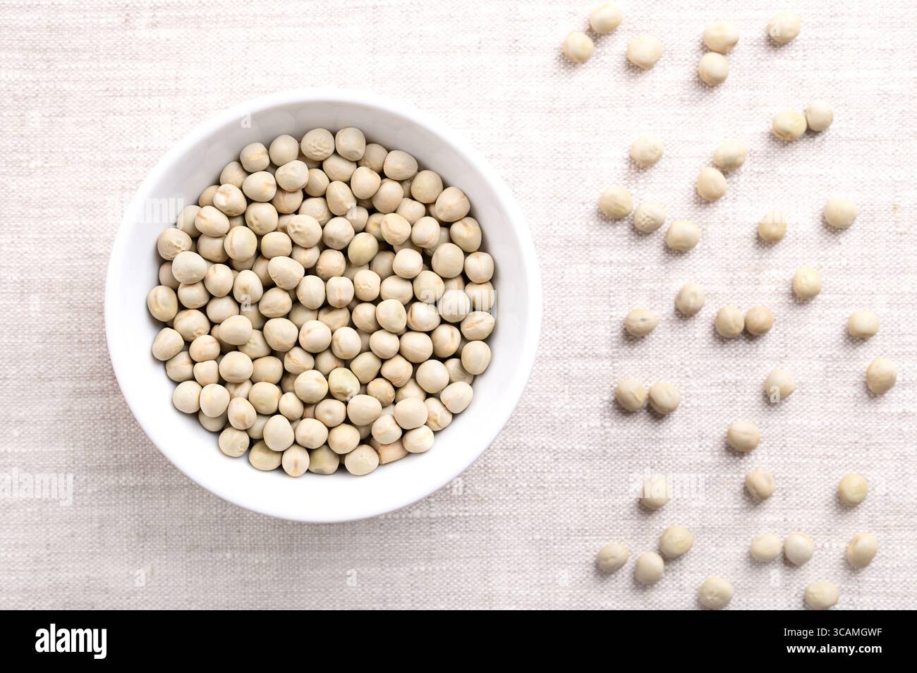 Pois verts séchés dans un bol blanc sur lin. Graines de Pisum sativum, légumineuses et fourragères, qui peuvent être reconstituées dans de l'eau chaude. Banque D'Images