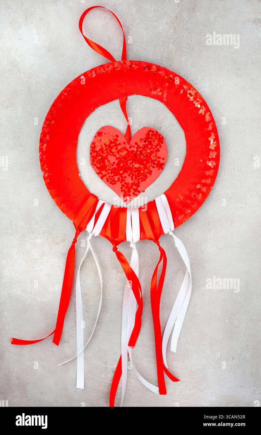 assiette en papier rouge avec coeur suspendu avec paillettes. le fond a des rubans rouges et blancs qui pendent de lui Banque D'Images