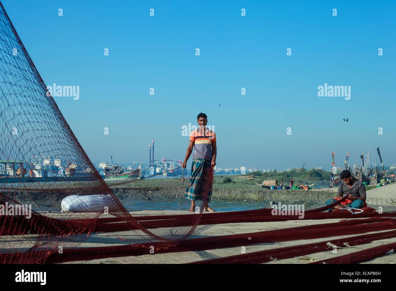 Chittagong, Bangladesh - 28 novembre 2019 : vue des pêcheurs au milieu des schémas complexes des filets de pêche, avec en toile de fond l'horizon côtier et des bateaux ancrés. Banque D'Images