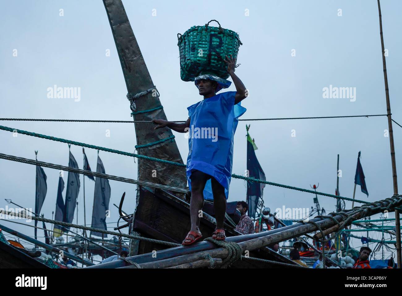 Chittagong, Bangladesh - 28 novembre 2019 : vue d'un homme en équilibre avec un panier vert, une figure frappante sur fond de bateaux de pêche. Banque D'Images