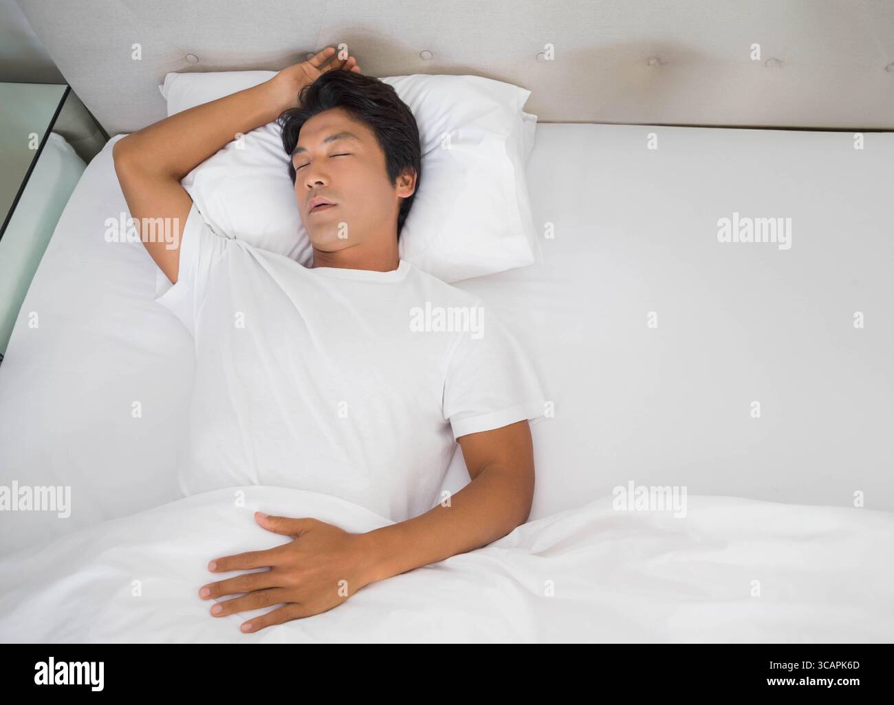 Homme japonais dormant dans la chambre à coucher, la tête reposant sur l'oreiller avec couette à côté de la table, espace copie Banque D'Images