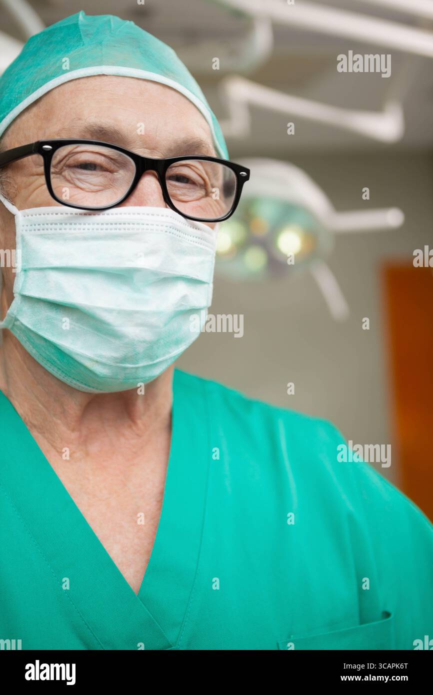 Chirurgien masculin senior portant des gommages verts, une casquette, un masque et des lunettes debout sous OU à la lumière Banque D'Images