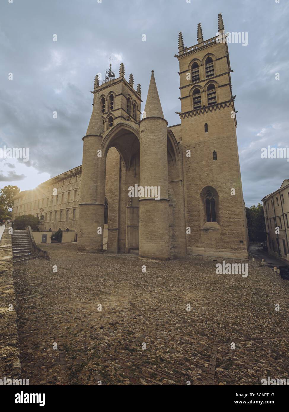 Vue sur une grande cathédrale aux flèches montantes et aux entrées voûtées, sa façade en pierre baignée de la lueur chaude du soleil couchant, Montpellier, Occitanie, France. Banque D'Images