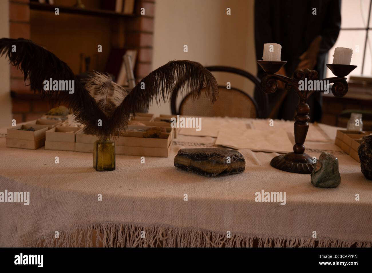 Une table d'étude vintage avec un bougeoir orné, des spécimens minéraux, des stylos à plume et de vieux documents, évoquant un coffret scientifique ou académique historique Banque D'Images