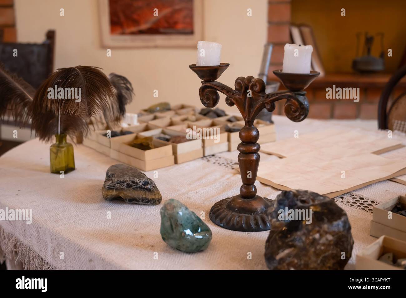 Une table d'étude vintage avec un bougeoir orné, des spécimens minéraux, des stylos à plume et de vieux documents, évoquant un coffret scientifique ou académique historique Banque D'Images