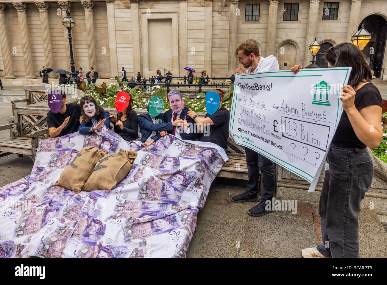 Londres, Royaume-Uni. 07 AOÛT 2025. Les gens détiennent un chèque géant envers des gens habillés en Rachel Reeves et Keir Starmer, alors que des militants de divers groupes, y compris les organisations à but non lucratif, positive Money et Tax Justice UK, ont mis en scène une cascade humoristique devant la Banque d'Angleterre. Exhortant le gouvernement à « sortir du lit » avec les banques, ils ont appelé les banques à être taxées davantage, avant la décision d'aujourd'hui de la Banque d'Angleterre sur les taux. Crédit Milo Chandler/Alamy Live News Banque D'Images