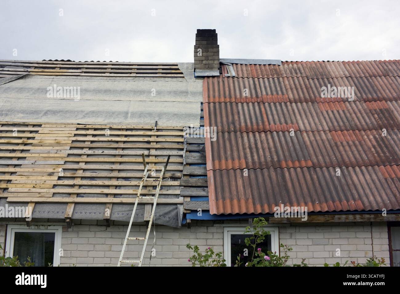 Réparation du toit de l'ancienne grange du village. Une moitié du toit est démontée aux planches et la seconde est recouverte de tuiles rouges Banque D'Images