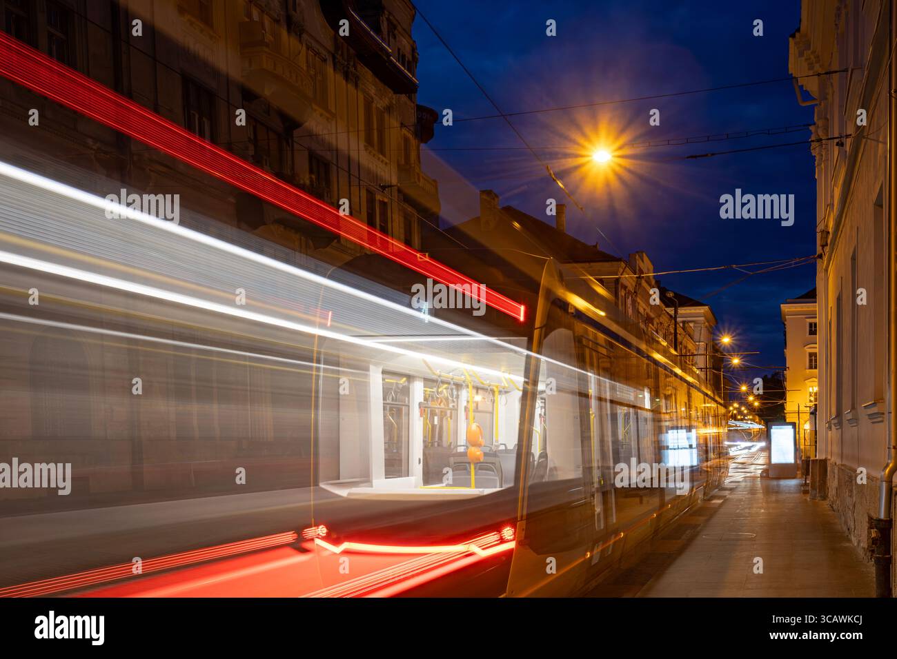 Prise de vue nocturne longue exposition des traînées de lumière du tramway courbant à travers le vieux centre-ville de Timisoara, Roumanie. Photo prise le 30 juillet 2025. Banque D'Images