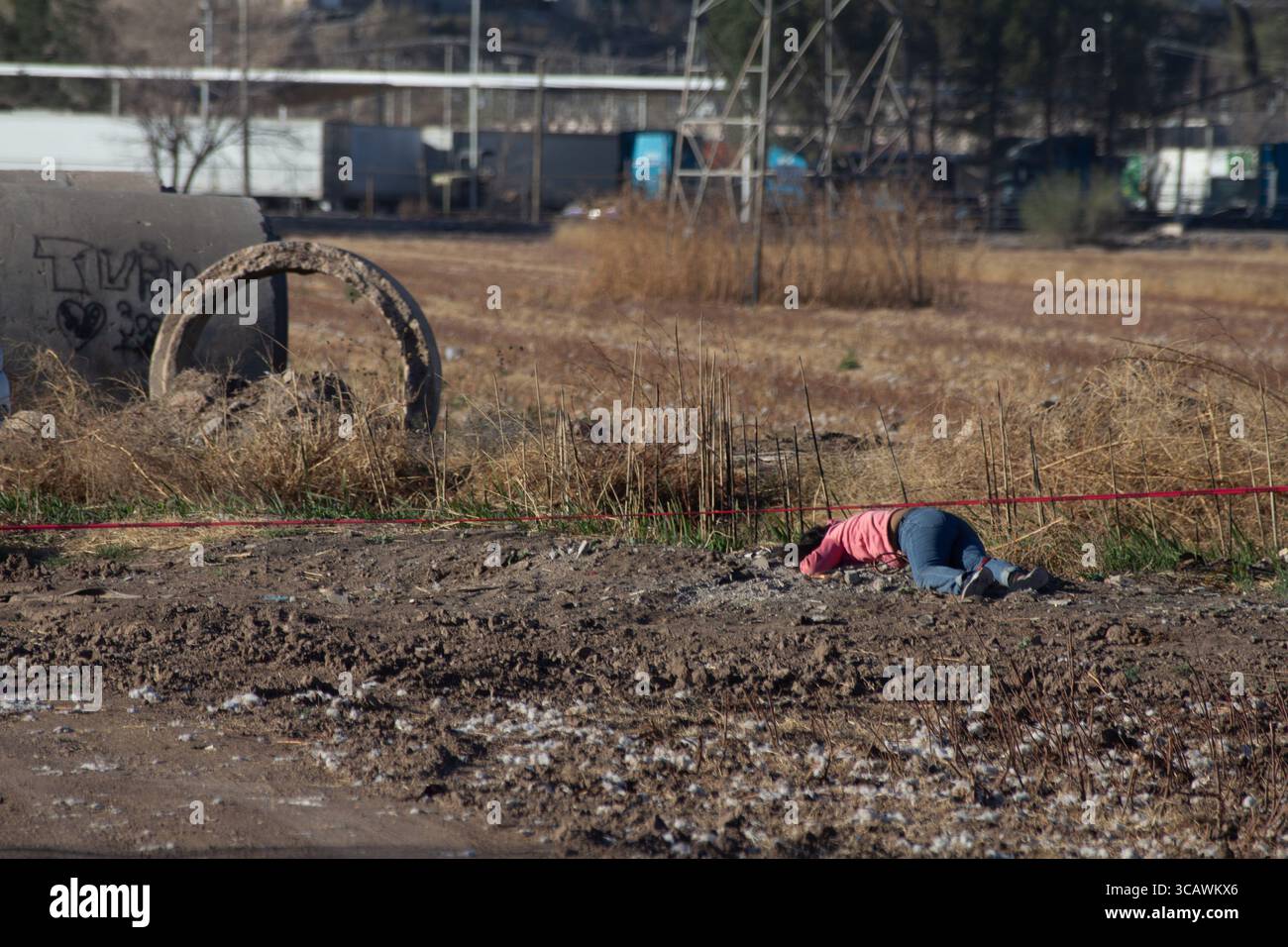 Une personne est exposée à un sol boueux à Ciudad Juarez, soulignant l'impact brutal de la violence urbaine avec la décomposition industrielle qui se profile en toile de fond. Banque D'Images