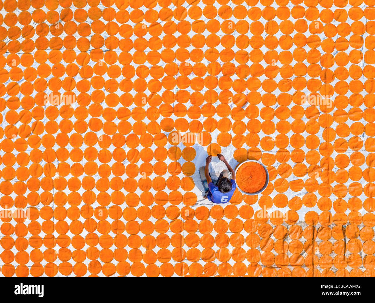 Bogura, Bangladesh - 05 février 2019 : vue aérienne d'une personne au milieu d'une mer de cercles orange vibrants séchant sous le soleil, créant un contraste saisissant avec la surface blanche. Banque D'Images