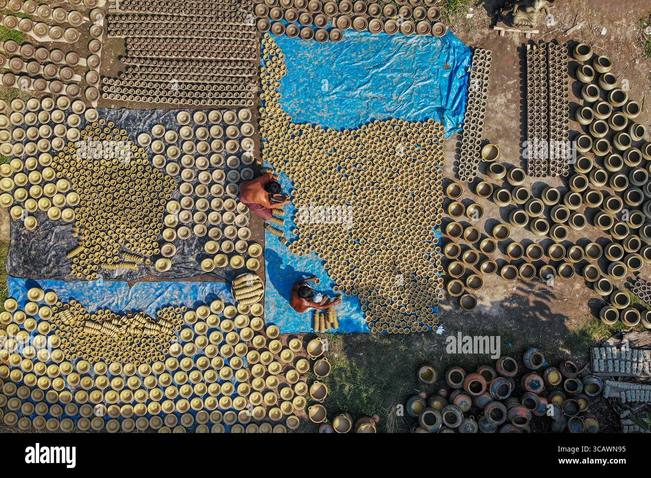Bogura, Bangladesh - 22 octobre 2019 : vue aérienne de pots de terre séchant sous le soleil, leurs formes circulaires créant des motifs contre la bâche bleue et le sol terreux. Banque D'Images
