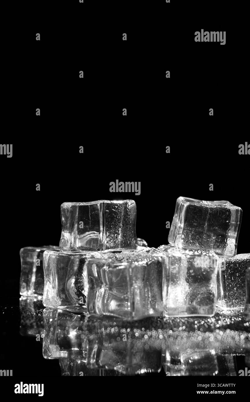 Un gros plan de plusieurs glaçons transparents réfléchissant sur une surface sombre et réfléchissante, Banque D'Images