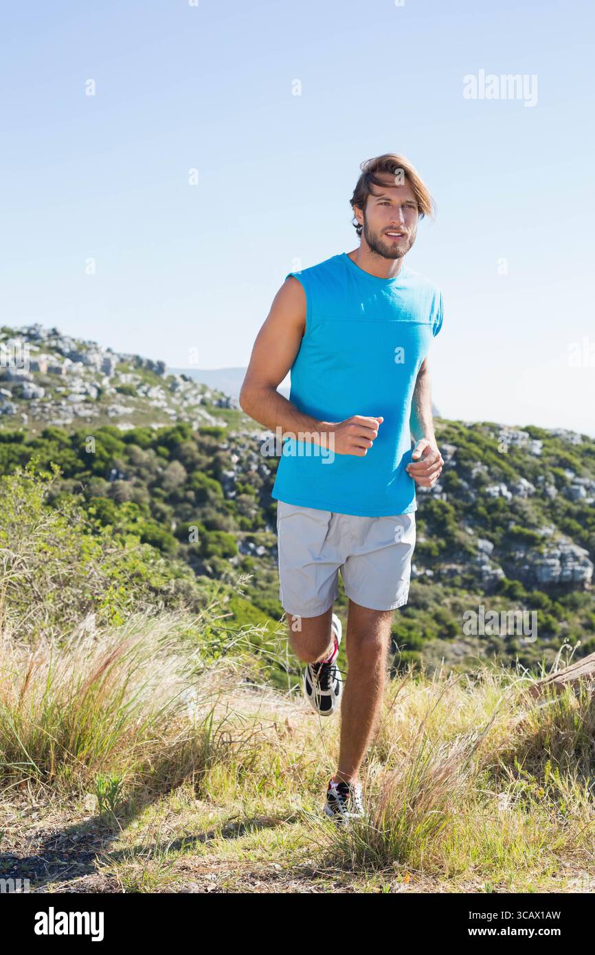 Homme du milieu des années 2020 qui monte sur une piste herbeuse à flanc de colline portant des chaussures de course à pied shorts bleus et gris Banque D'Images