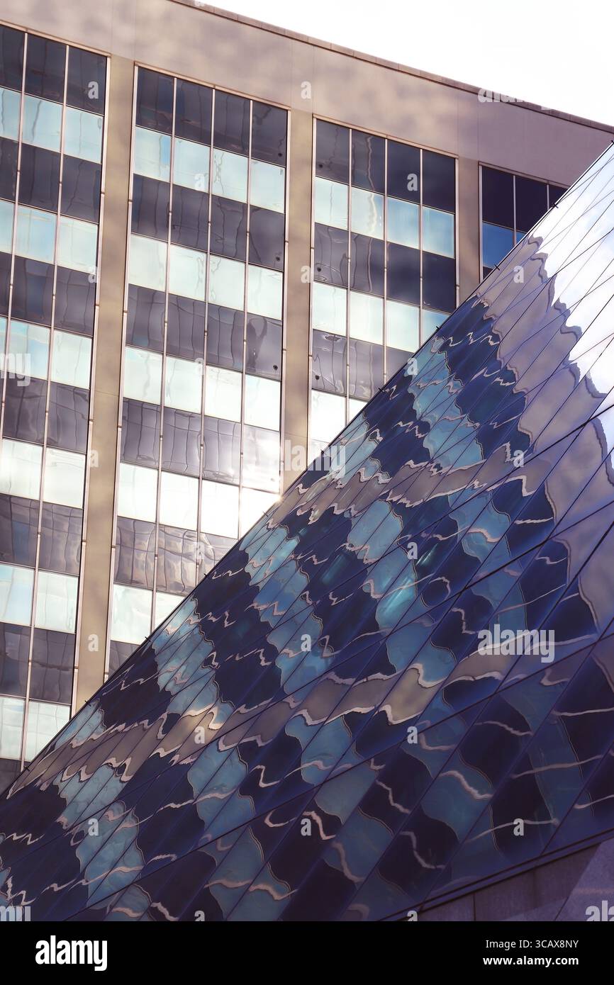 Deux bâtiments se réunissant en une ligne diagonale pointue avec un motif de grille de fenêtres rectangulaires réfléchissant dans la surface vitrée du bâtiment diagonal Banque D'Images