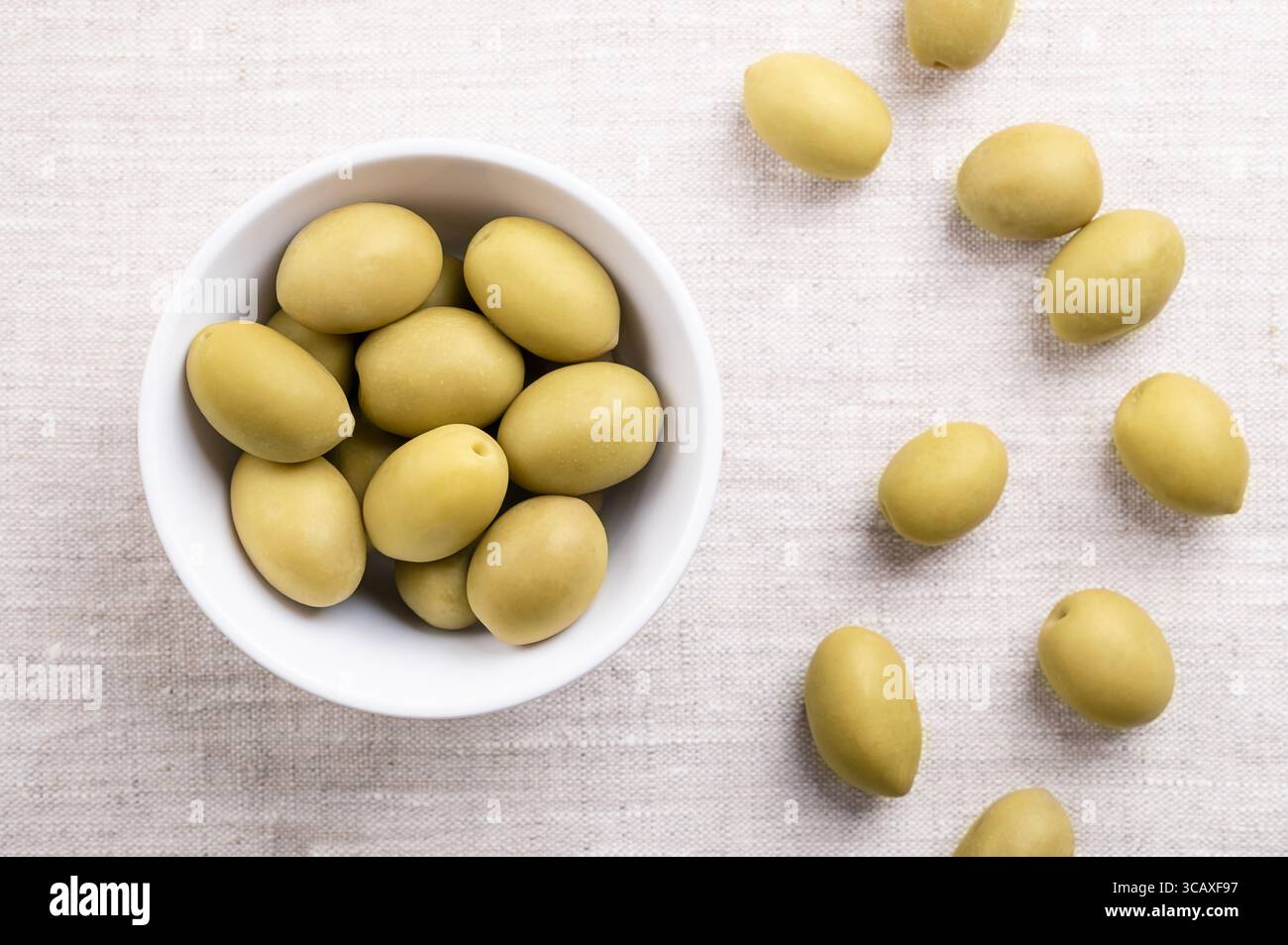 Olives vertes avec fosse, dans un bol blanc sur lin. Olives de table entières, grandes, récoltées avant d'être complètement mûres, avec une saveur plus acidulée et saumeuse. Banque D'Images