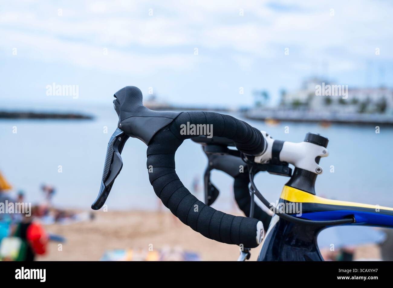Un vélo avec un guidon noir et jaune est garé sur une plage. Le guidon est enveloppé dans un matériau noir et jaune. Banque D'Images