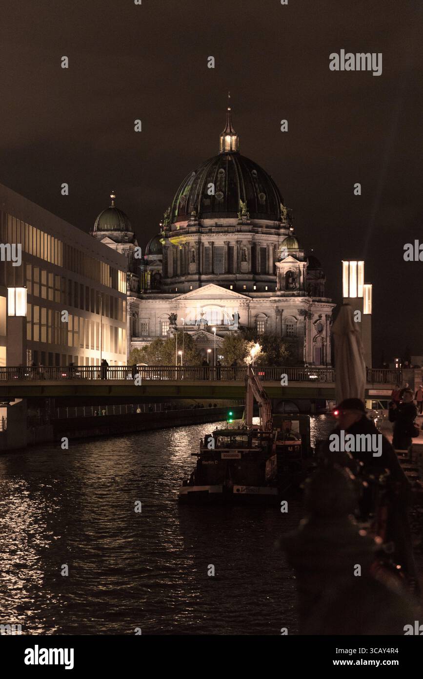 Vue nocturne de la cathédrale de Berlin illuminée de lumières chaudes reflétant la rivière Spree et le paysage urbain en arrière-plan Banque D'Images