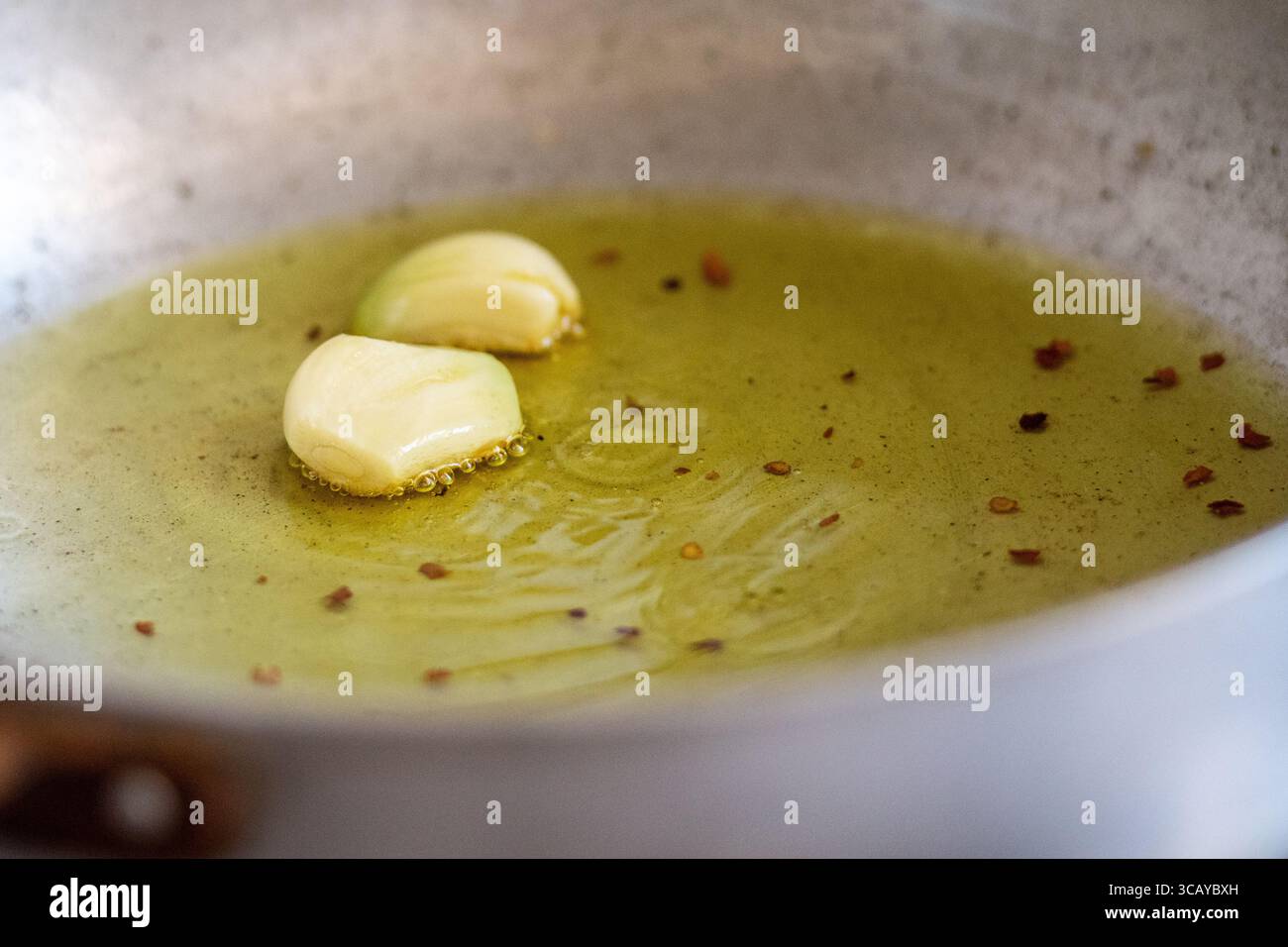 Gousses d'ail grésillant dans l'huile d'olive avec des flocons de piment dans une poêle. Une étape de cuisson maison classique pour infuser l'huile avec saveur Banque D'Images