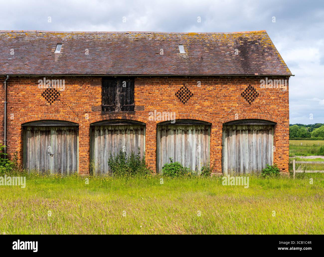 Une grange en briques altérées avec quatre portes en bois se trouve dans un champ dans la campagne anglaise du Shropshire Banque D'Images Une grange en briques altérées avec quatre portes en bois se trouve dans un champ dans la campagne anglaise du Shropshire Banque D'Images