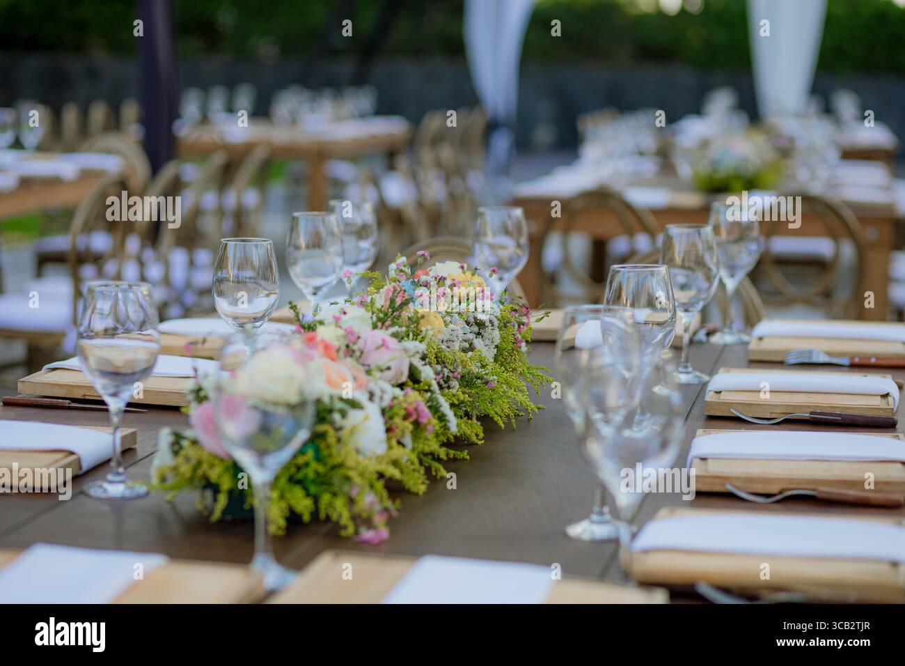 Table en bois décorée avec des verres en cristal et une pièce maîtresse florale, placée à l'extérieur pour un mariage ou une célébration élégante. Banque D'Images