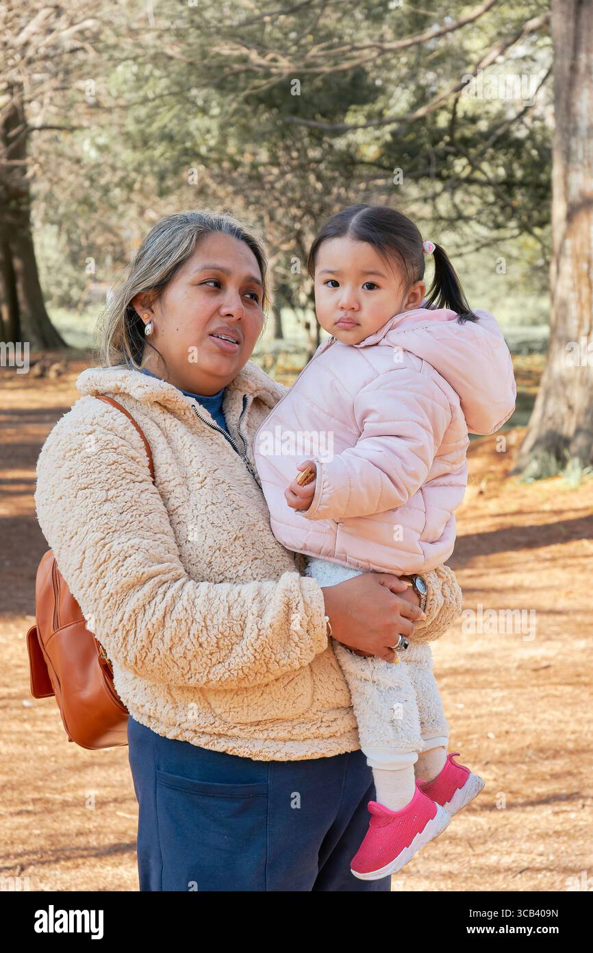 Mère tient sa fille dans une forêt d'automne. Les deux sont habillés chaudement ; elle porte une veste rose et des baskets, lui porte une veste beige. Un scen chaleureux et familier Banque D'Images