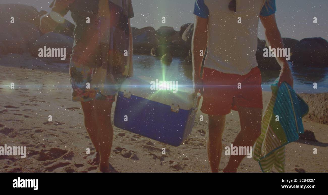 Marcher deux amis masculins portant glacière portable et serviette rayée sur le rivage de sable au coucher du soleil Banque D'Images