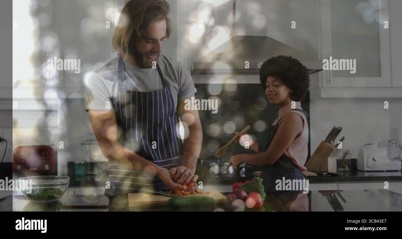 Homme portant tablier tranchant les carottes et femme remuant pot avec cuillère en bois dans la cuisine avec des légumes verts Banque D'Images