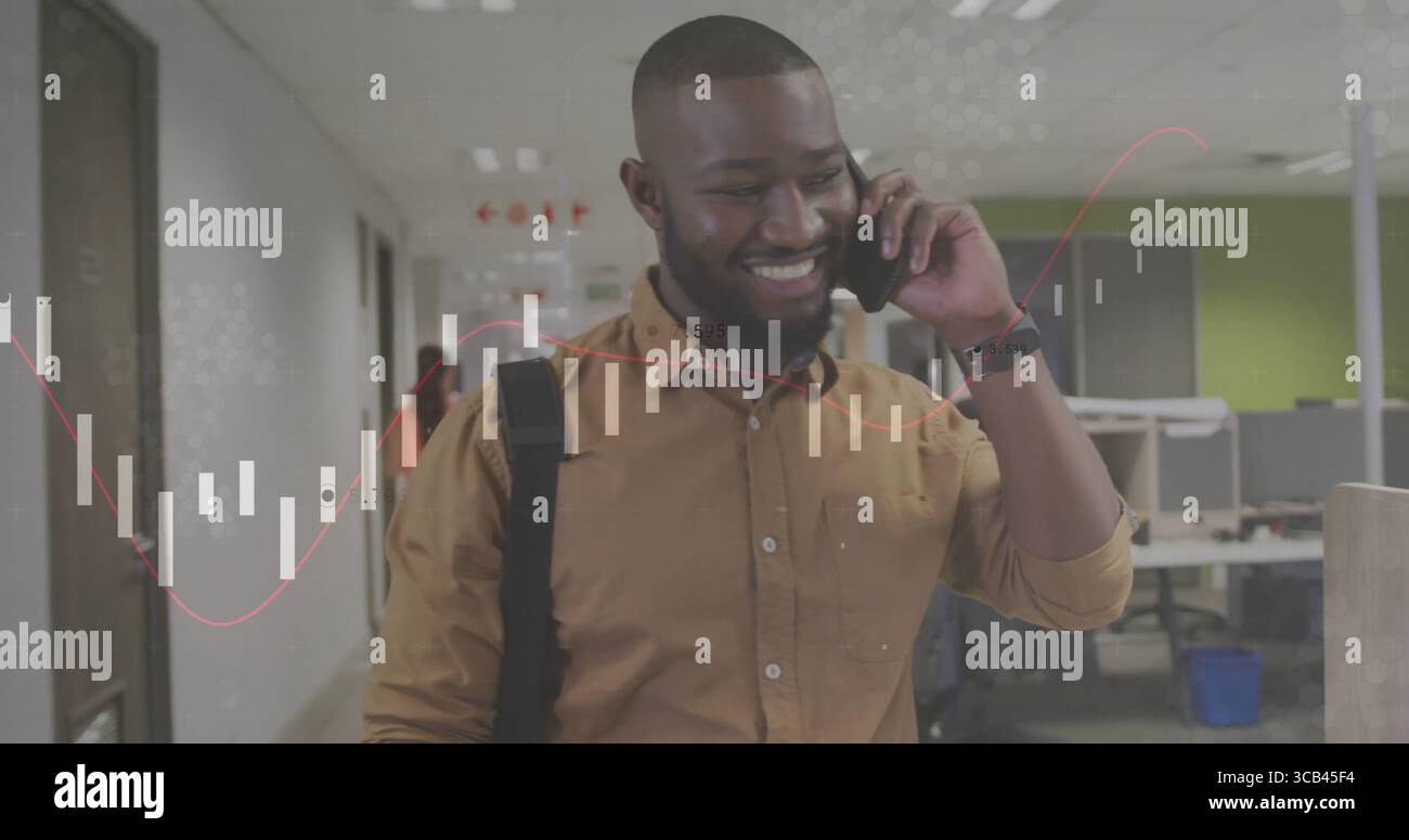 Homme marchant portant chemise moutarde et sac à dos à travers le couloir du bureau, parlant sur smartphone Banque D'Images