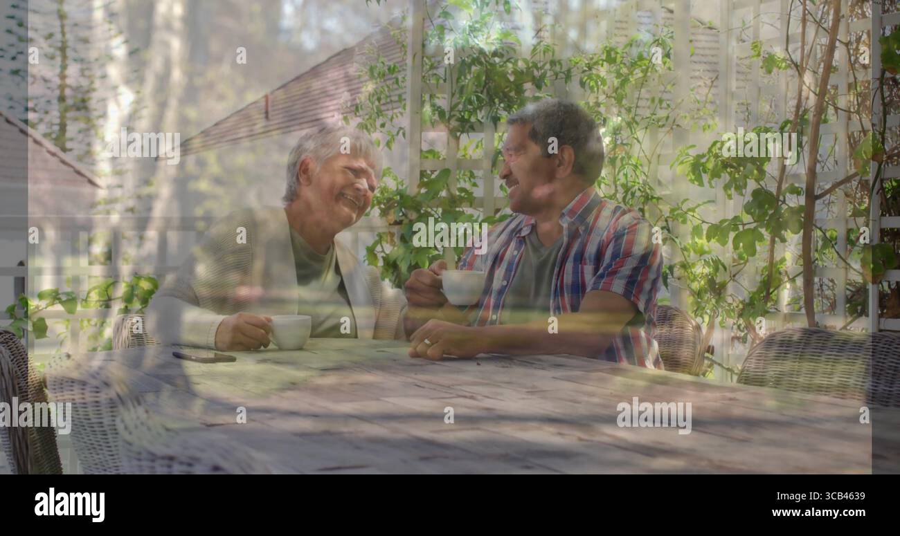 Siroter couple senior s'engageant dans la conversation à la table en bois sur le patio du jardin, avec des tasses en céramique Banque D'Images