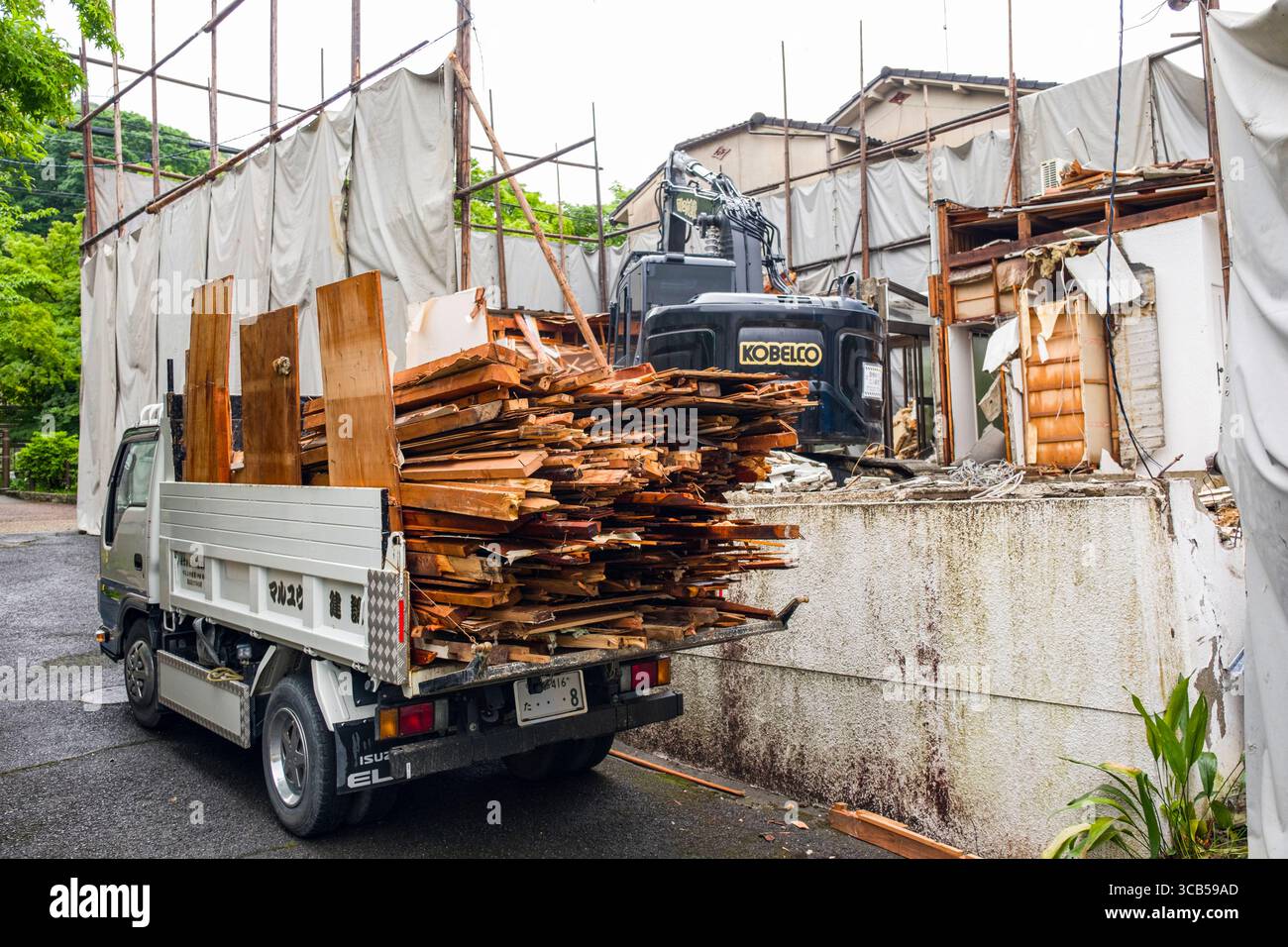 Un camion chargé de débris de bois se trouve sur un chantier de construction avec une excavatrice visible et un bâtiment partiellement démonté, Kyoto, Japon Banque D'Images