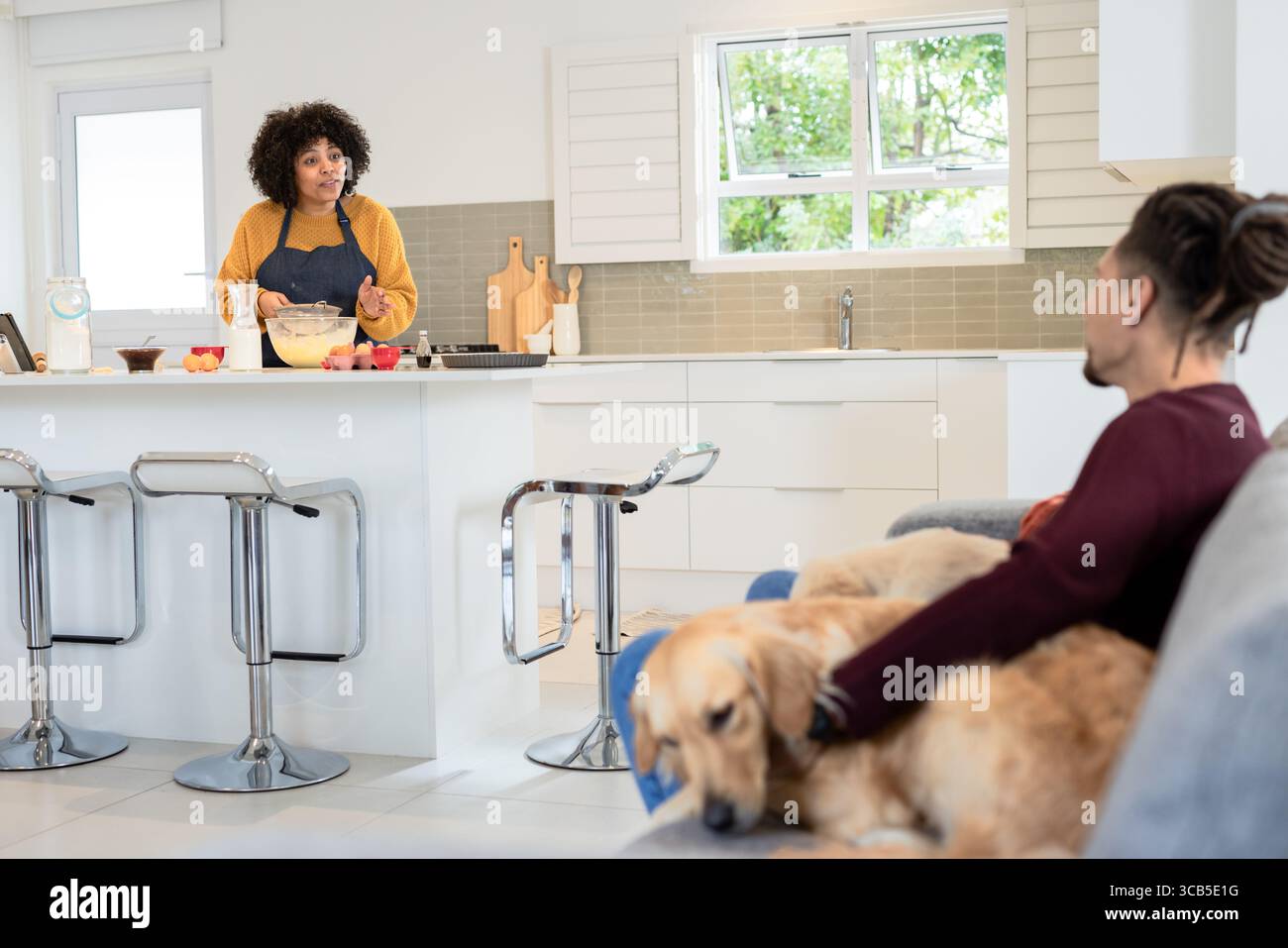 Couple diversifié mélangeant la pâte dans un bol en verre et chien caressant sur le canapé dans la cuisine, espace de copie Banque D'Images