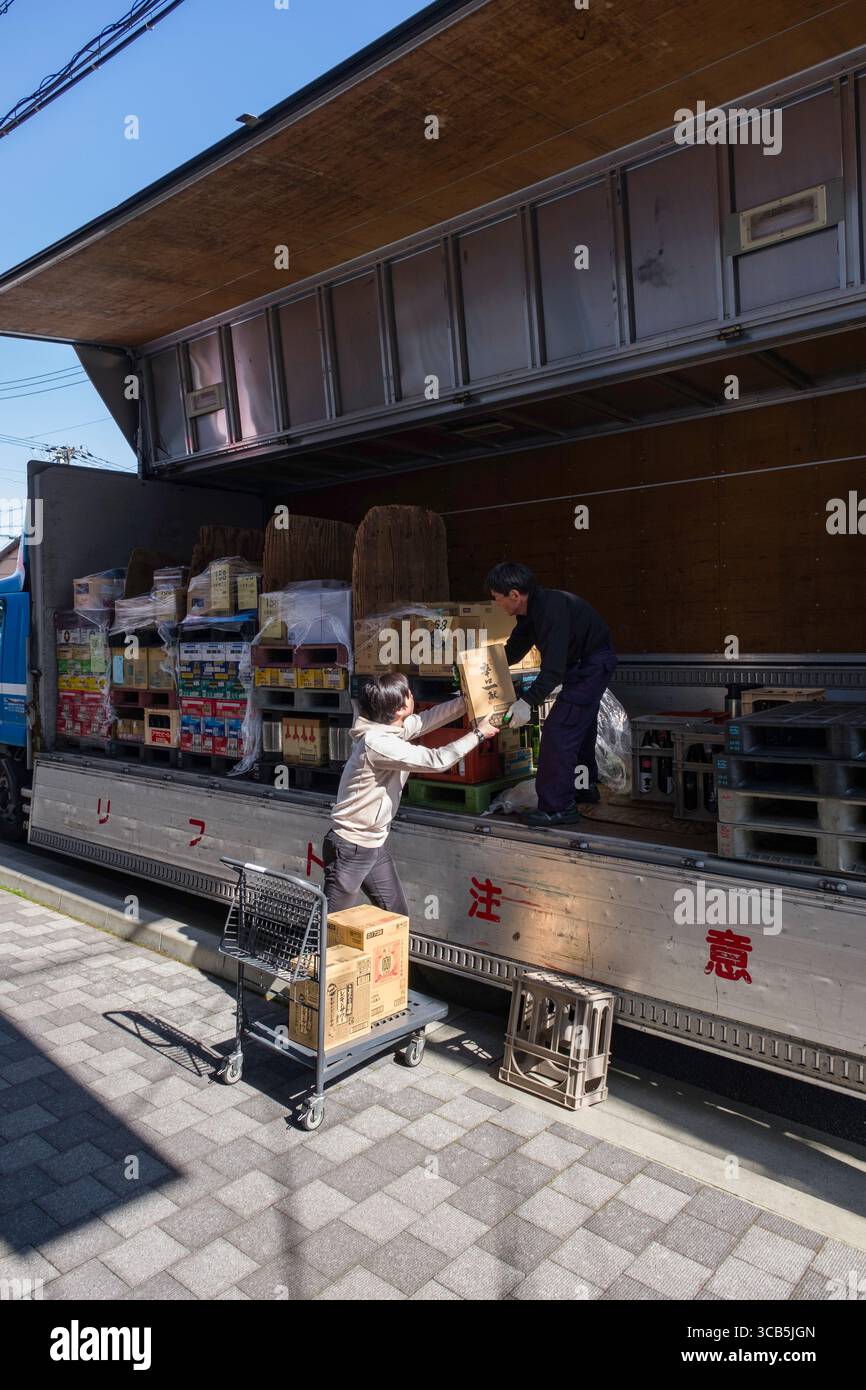 Deux ouvriers chargeant diverses boîtes dans un camion commercial à chargement latéral, mettant en valeur le travail d'équipe et l'efficacité dans la logistique. La scène capture l'essence Banque D'Images