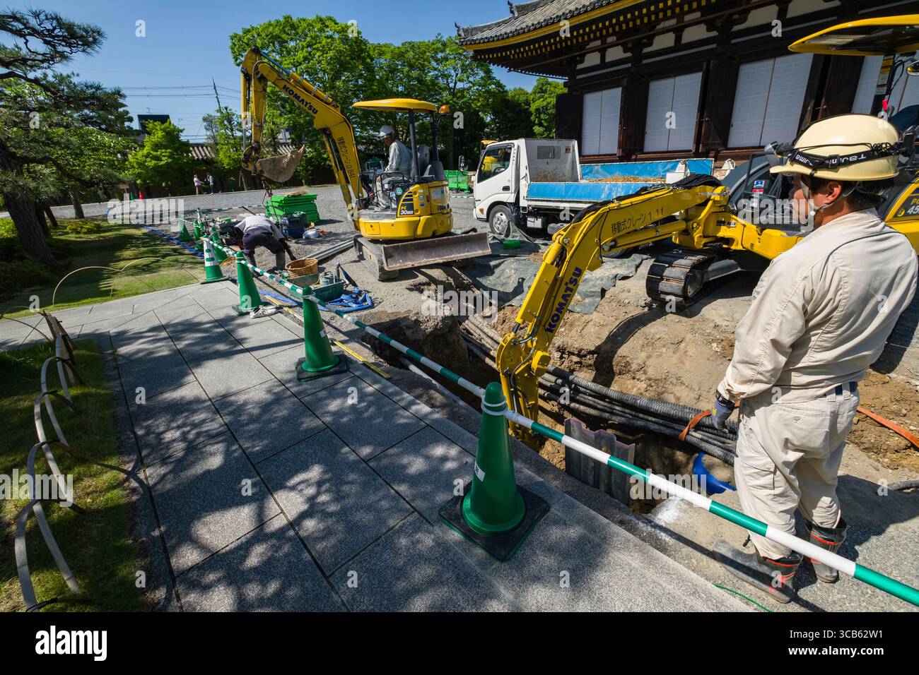 Les ouvriers du bâtiment utilisent de la machinerie lourde sur le chantier du temple Sanjūsangen-dō, entouré de cônes de sécurité et de verdure. La scène s'élève Banque D'Images