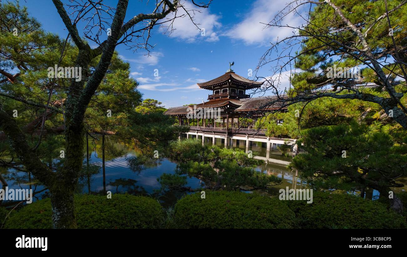Pavillon Heian Jingu Taiheikaku entouré de verdure et de reflets d'eau tranquilles sous un ciel bleu vif, capturant l'harmonie du traditi Banque D'Images