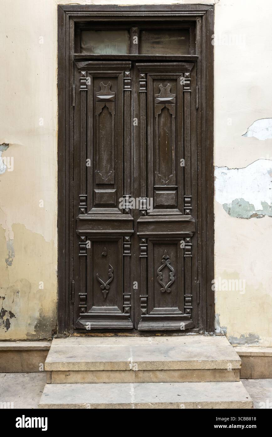 Vue détaillée d'une porte en bois antique artistique avec des sculptures décoratives, élégamment serrée contre un mur en stuc altéré. Vue de face, phot d'arrière-plan Banque D'Images