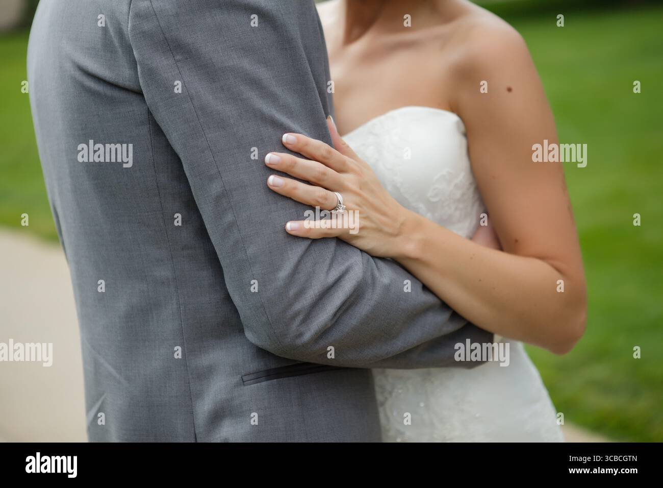 Mariée embrasse le bras du marié, soulignant l'anneau de mariage et l'amour Banque D'Images